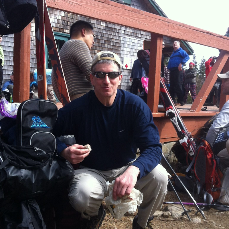 Kulkea founder kneeling with ski boot bag on mountain